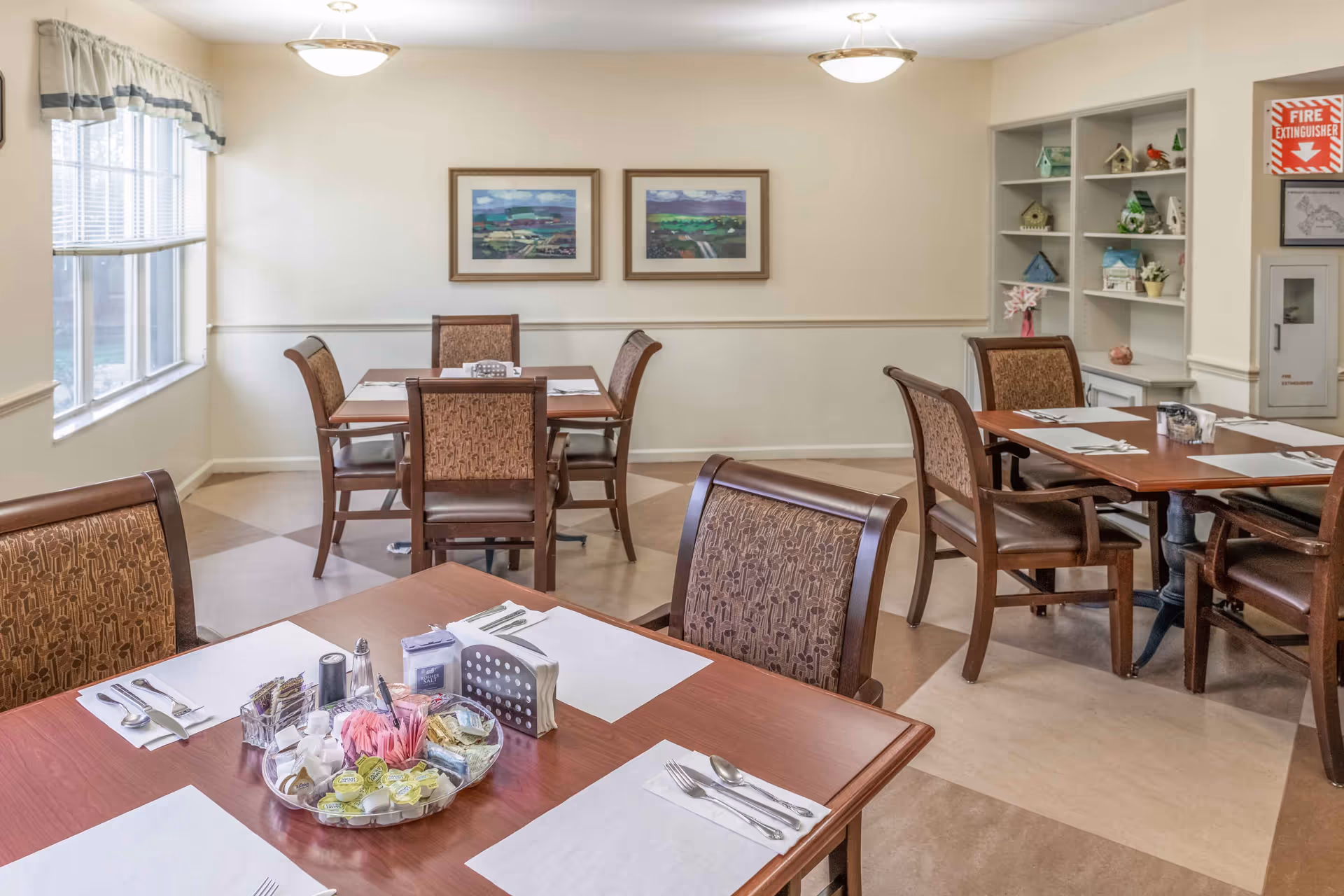 Bright dining room with multiple set tables and chairs, wall art, and a window.