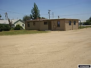 Small beige single-story building on a dirt lot with utility poles nearby.
