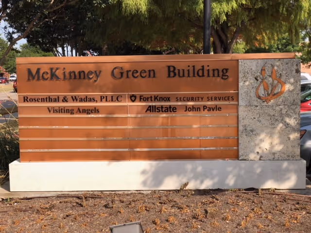 Outdoor sign on a concrete base reads McKinney Green Building with tenant names.