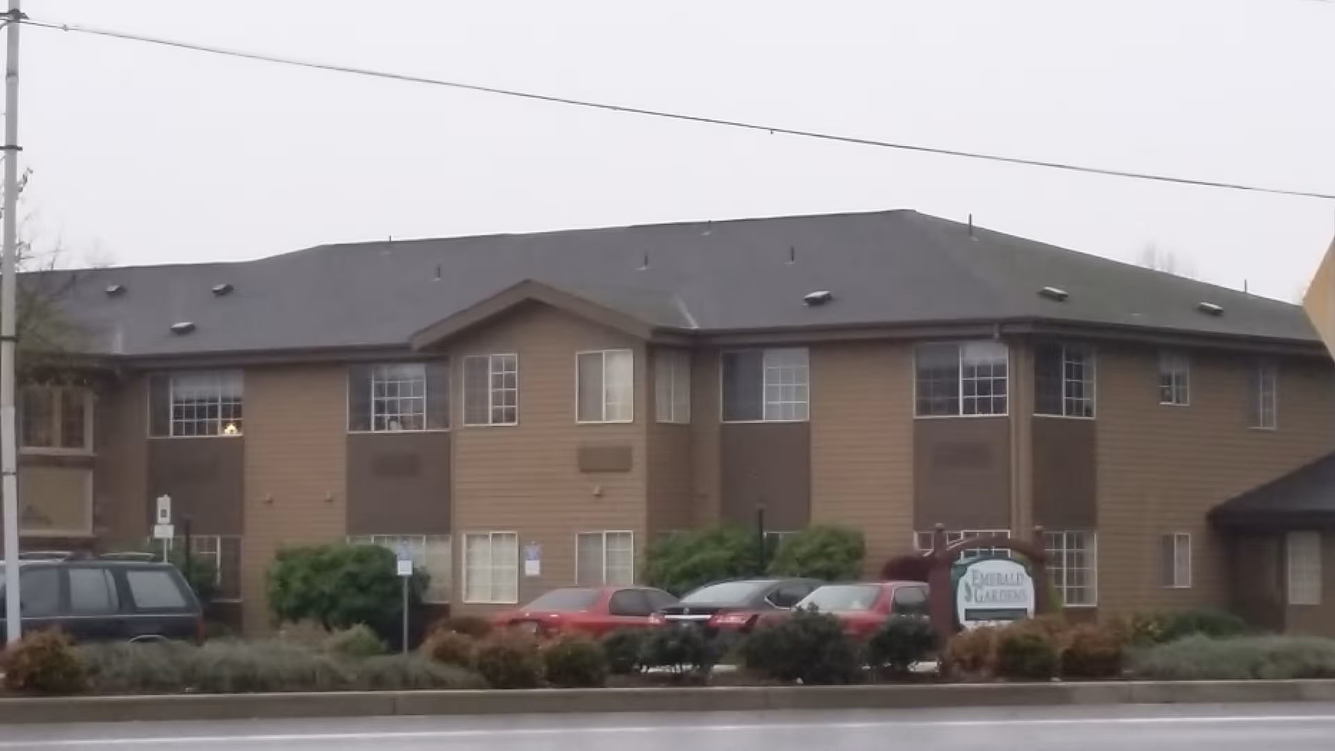 Exterior view of Emerald Gardens senior living facility with parked cars and landscaping.