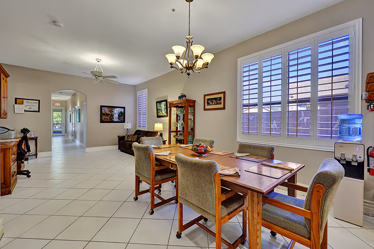 Bright dining room with a wooden table, upholstered chairs, large windows, and a water cooler.