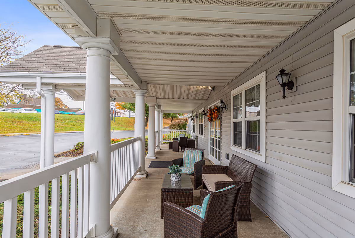 Covered outdoor porch with wicker chairs and tables along the building at Allegheny Place.