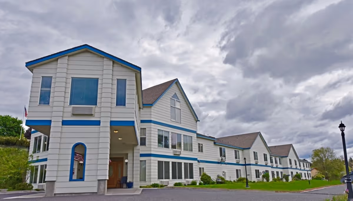 White senior living facility with blue trim, connected units, and a prominent front entrance.