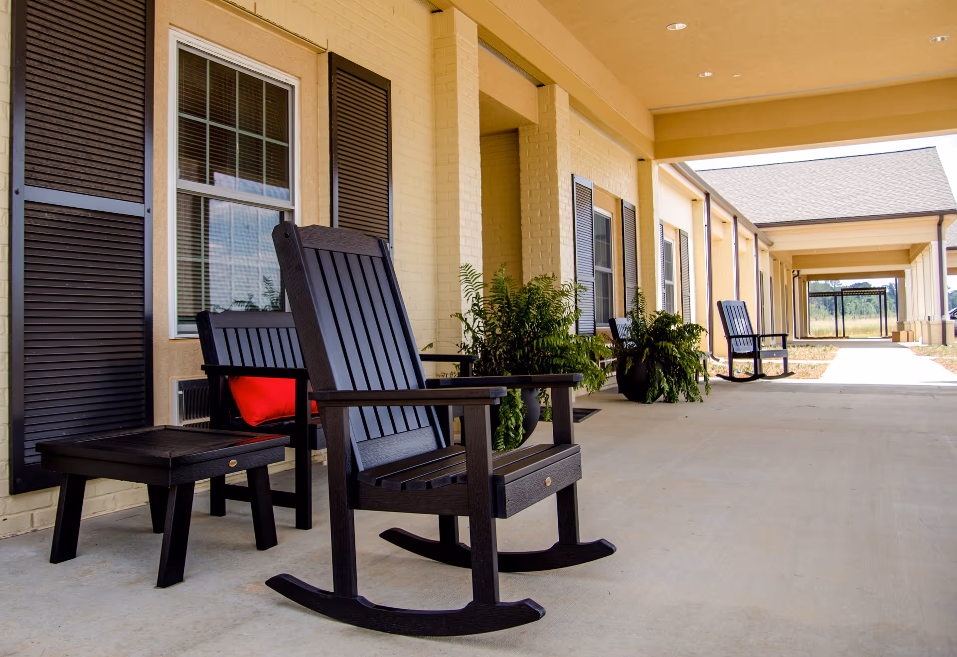 Covered exterior walkway at UpsideHoM Lighthouse Point with rocking chairs and plants.