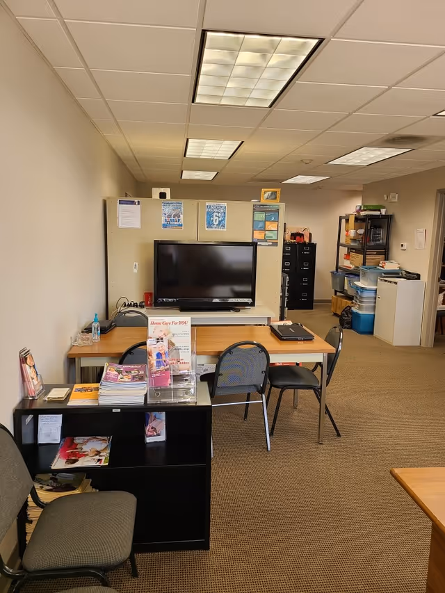 A small office area inside a senior care facility with desks, chairs, and a TV.