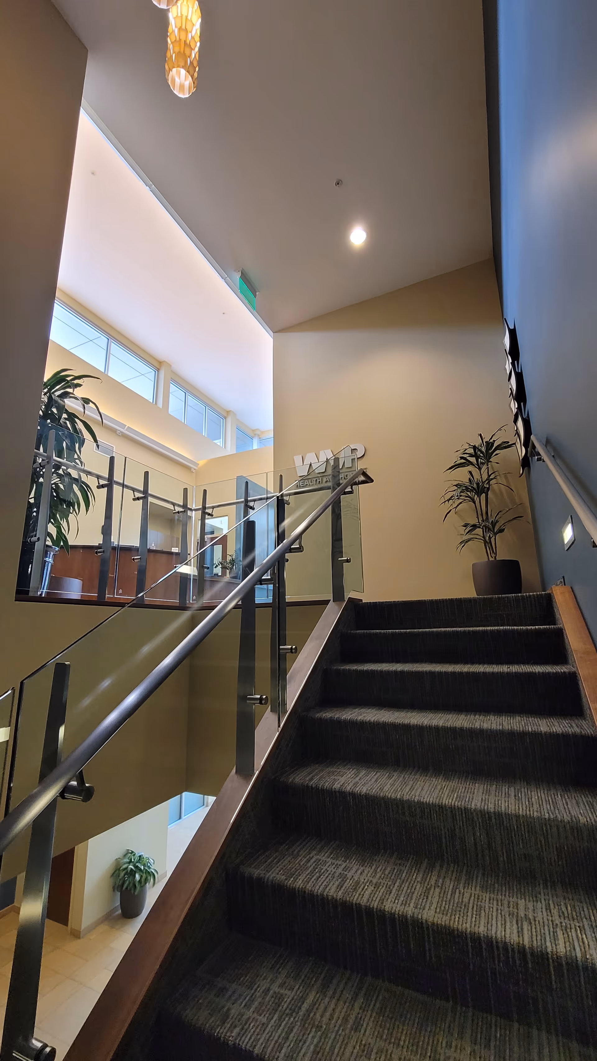 Interior staircase in a senior living facility with glass railing and potted plants.