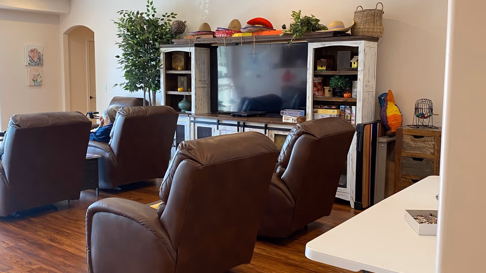 Residents sit in brown recliners watching a large TV in a cozy living room.