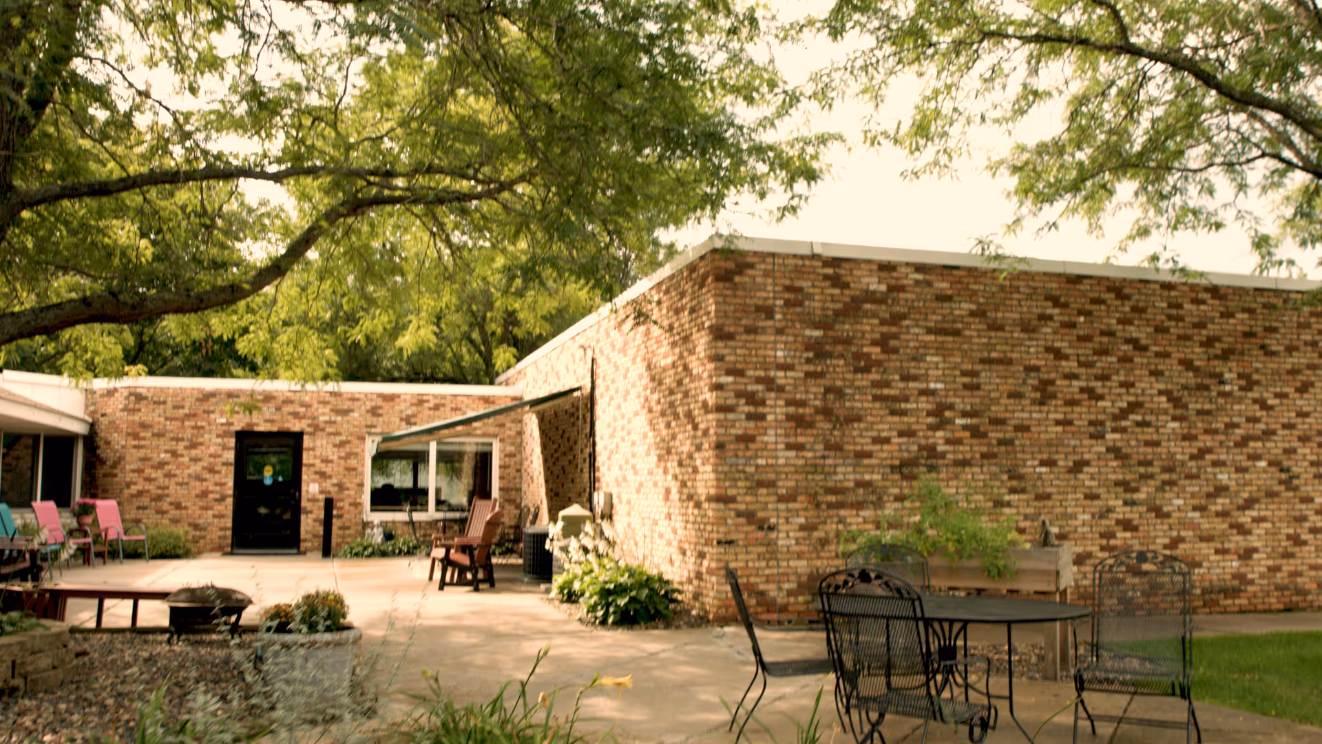 Brick exterior with a sunny outdoor patio, tables, chairs, and planters.