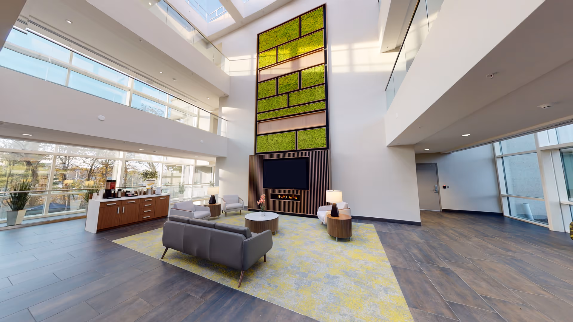 Spacious multi-story lobby with seating, large windows, a green vertical wall, TV/fireplace and a coffee station.