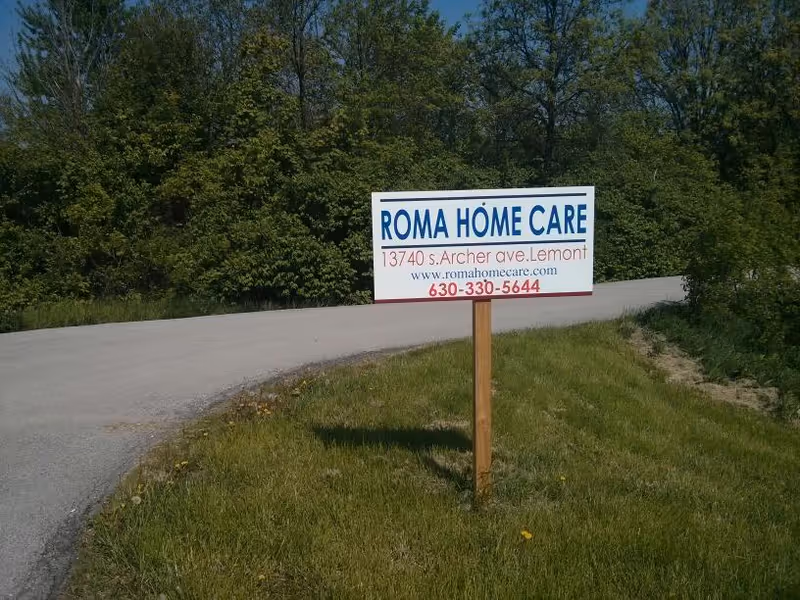 Sign for Roma Home Care on a grassy roadside with trees in background.