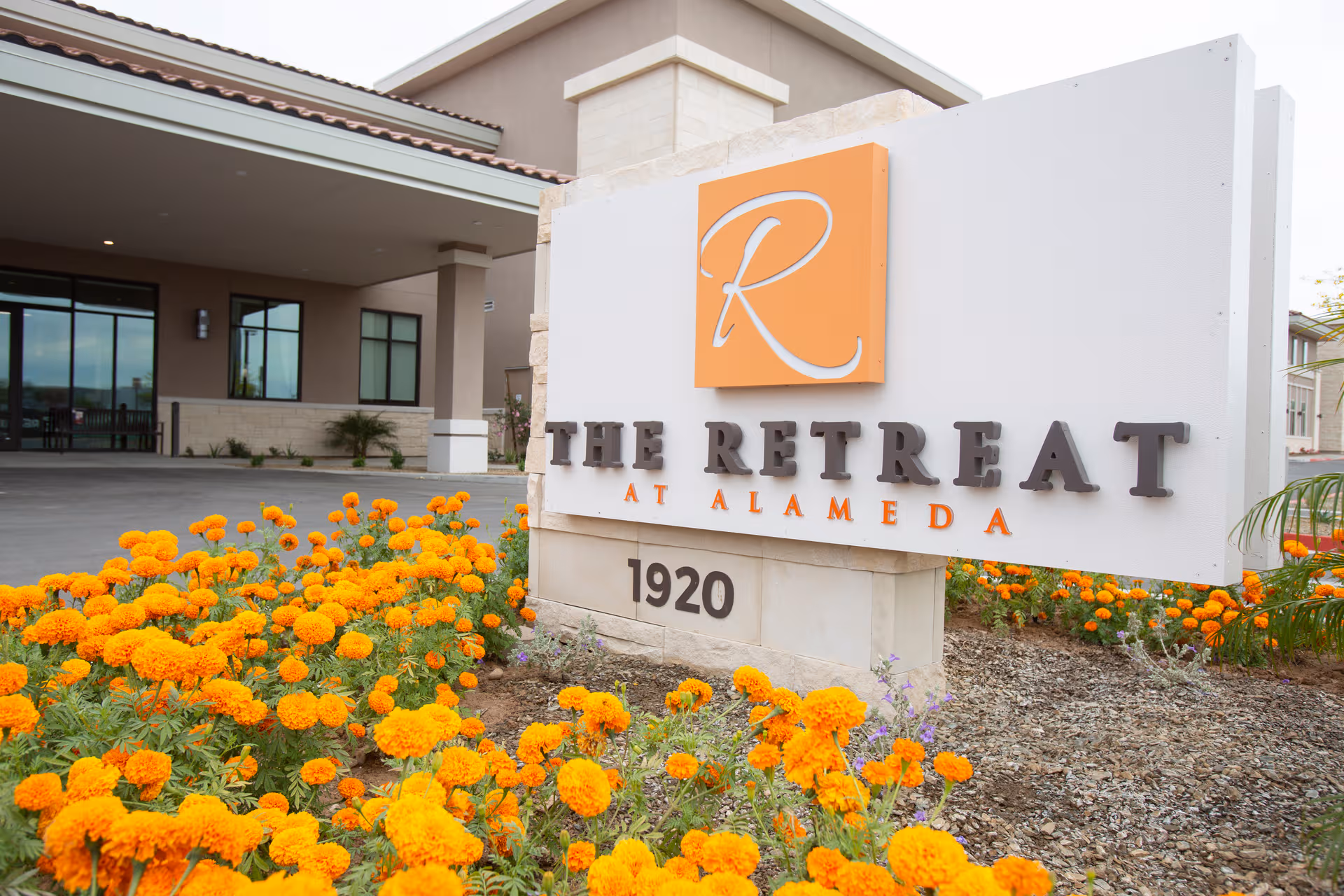 A large sign reading The Retreat at Alameda stands amid orange marigolds at the entrance.