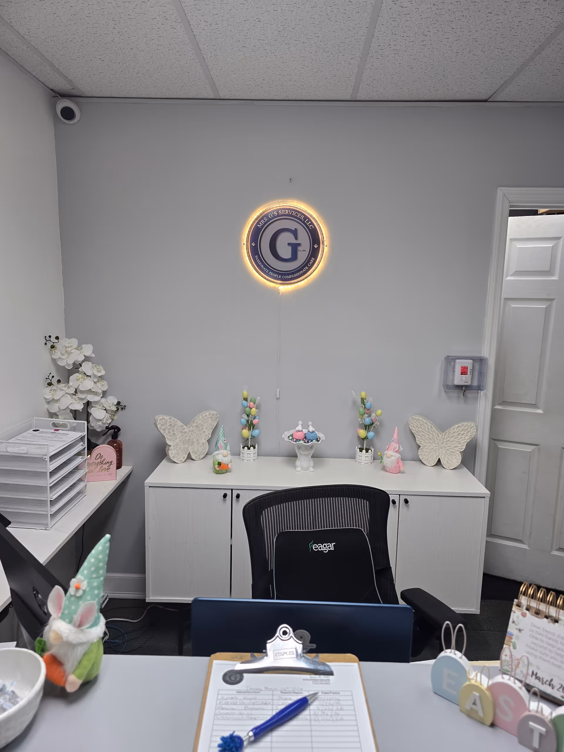 Office reception area with illuminated round logo, pastel decor, and desk with chair.