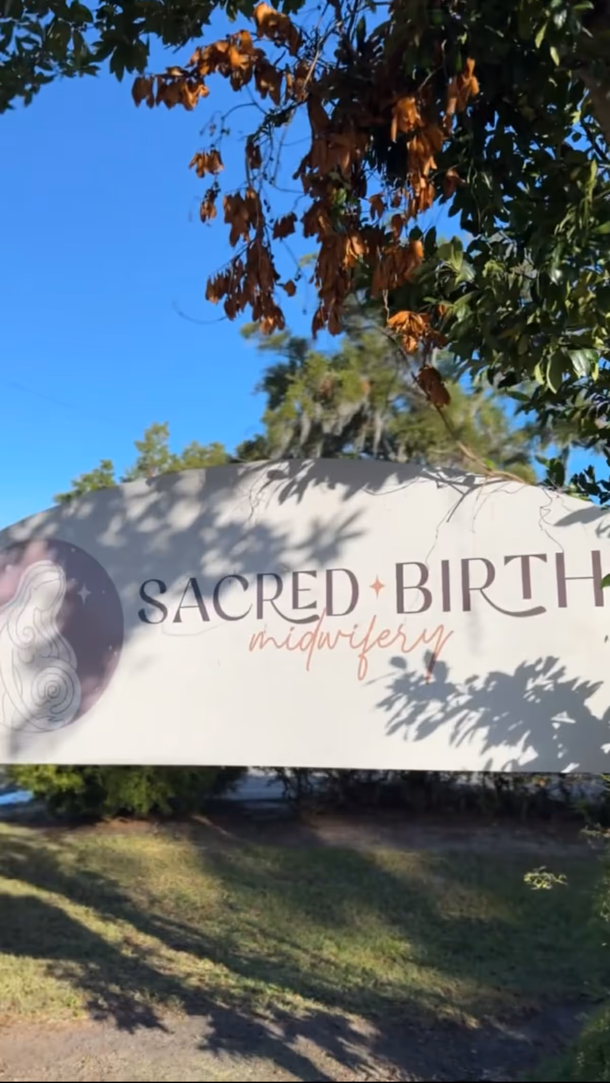 Outdoor view of Sacred Birth Midwifery sign with trees and blue sky.