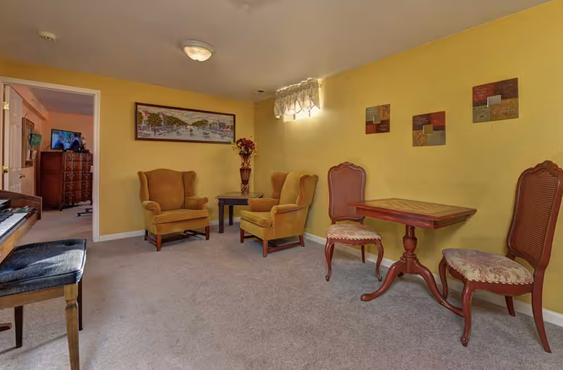 Yellow walls in a living room with vintage chairs, a piano, and a small table.