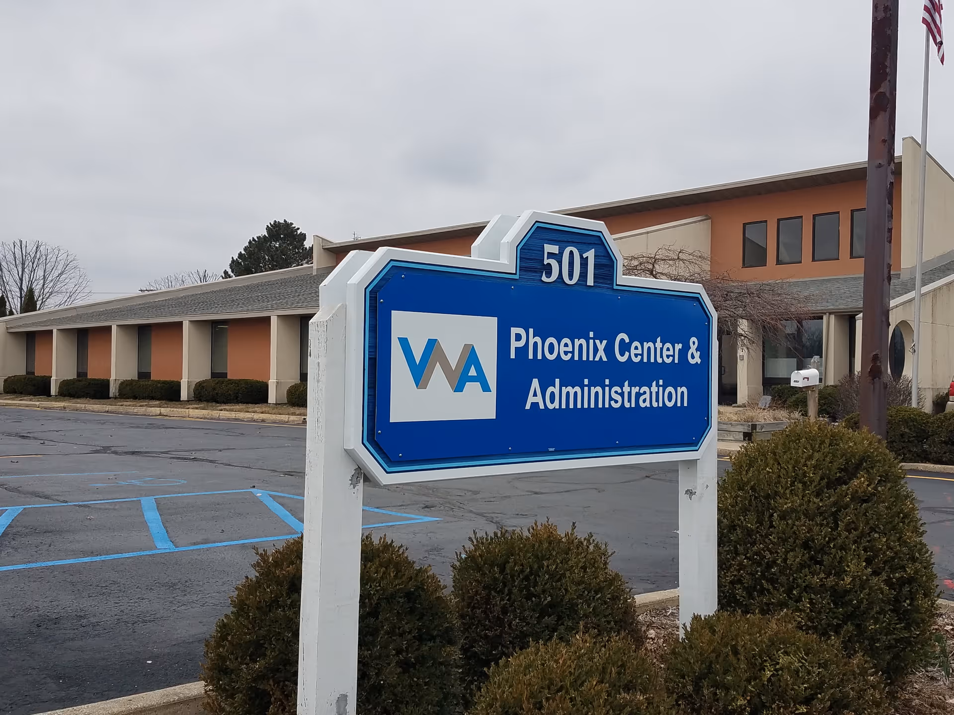 Blue sign reading Phoenix Center & Administration in foreground with beige building and parking lot.