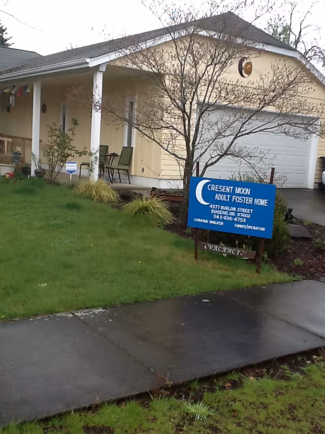 Yellow single-story Crescent Moon Adult Foster Home exterior with front porch and blue sign.