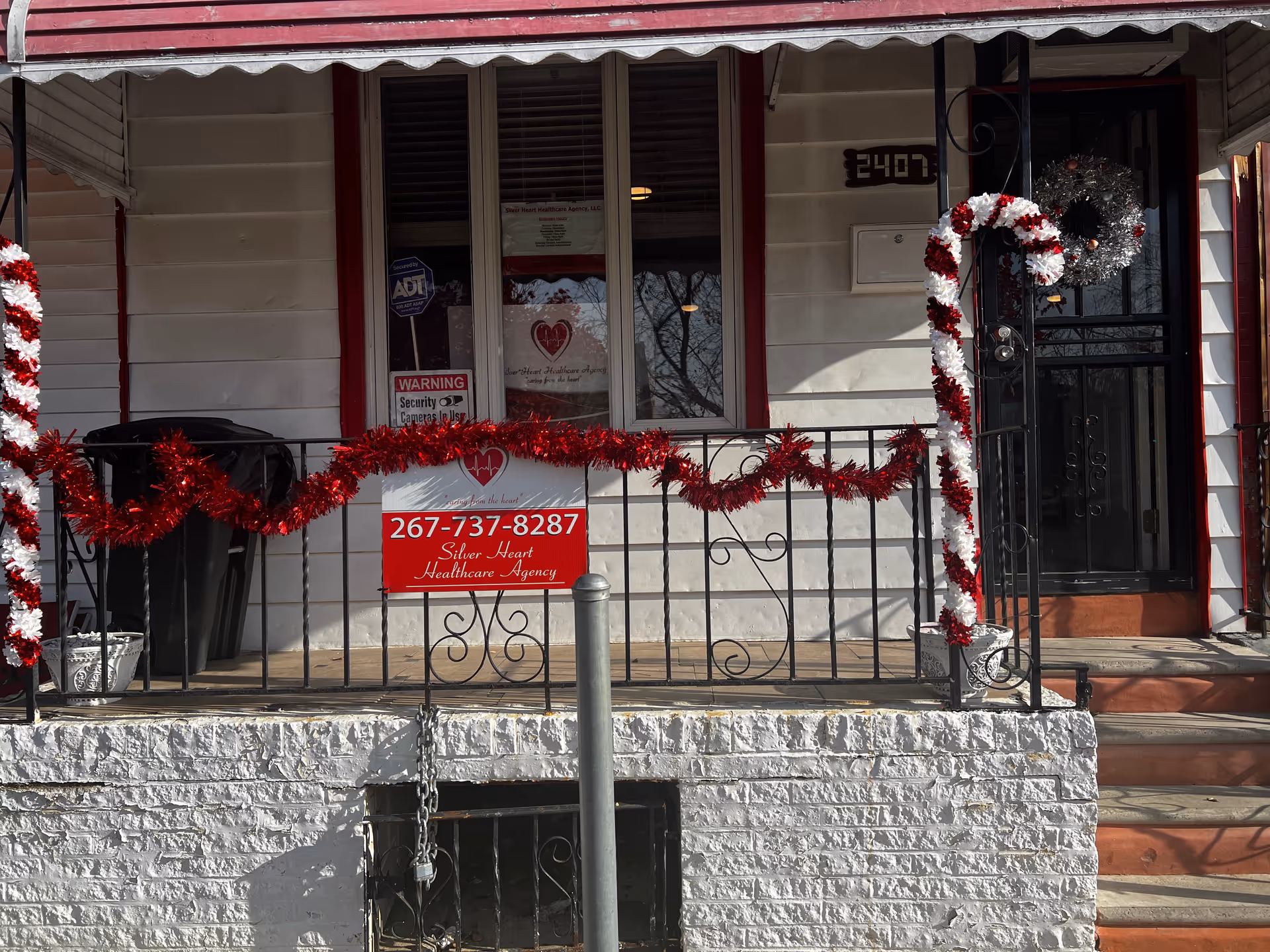 Front exterior of Silver Heart Healthcare Agency with red garlands and a sign on the railing.