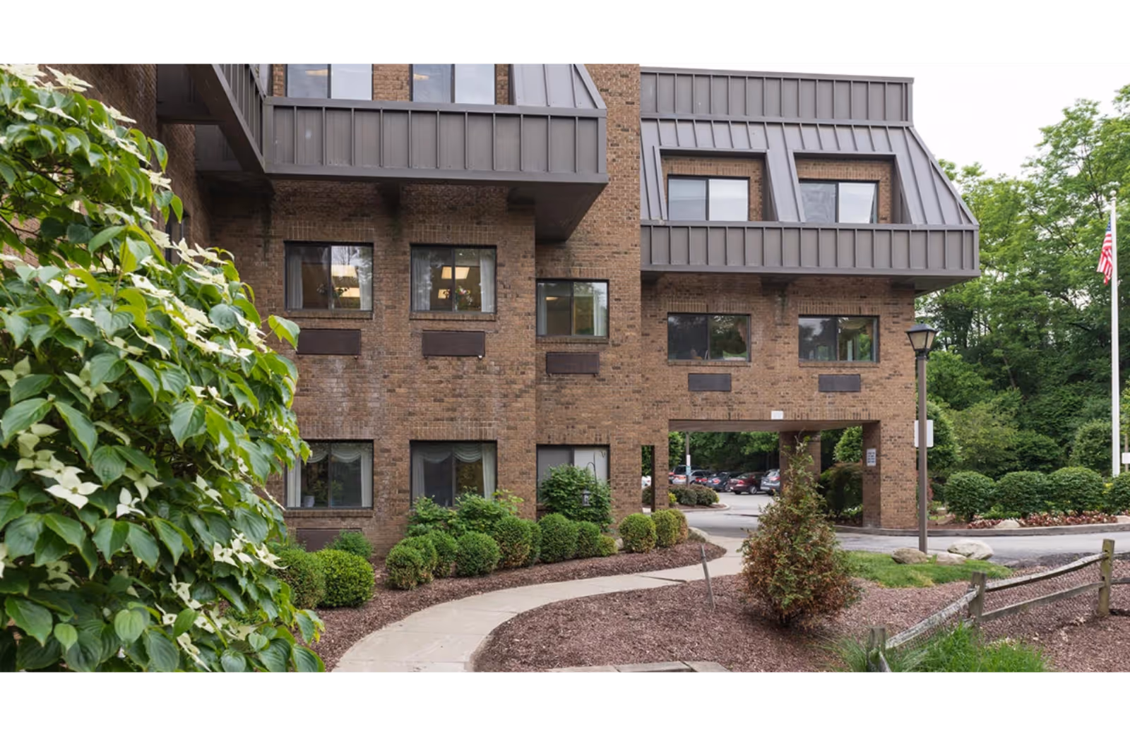 Brick senior living building with landscaped entrance and archway, surrounded by shrubs.