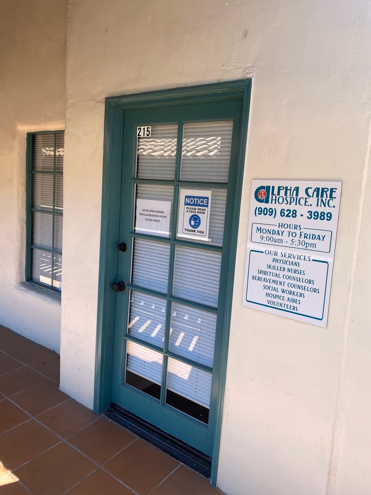 Teal-framed glass door with notices and an Alpha Care Hospice sign on exterior wall.