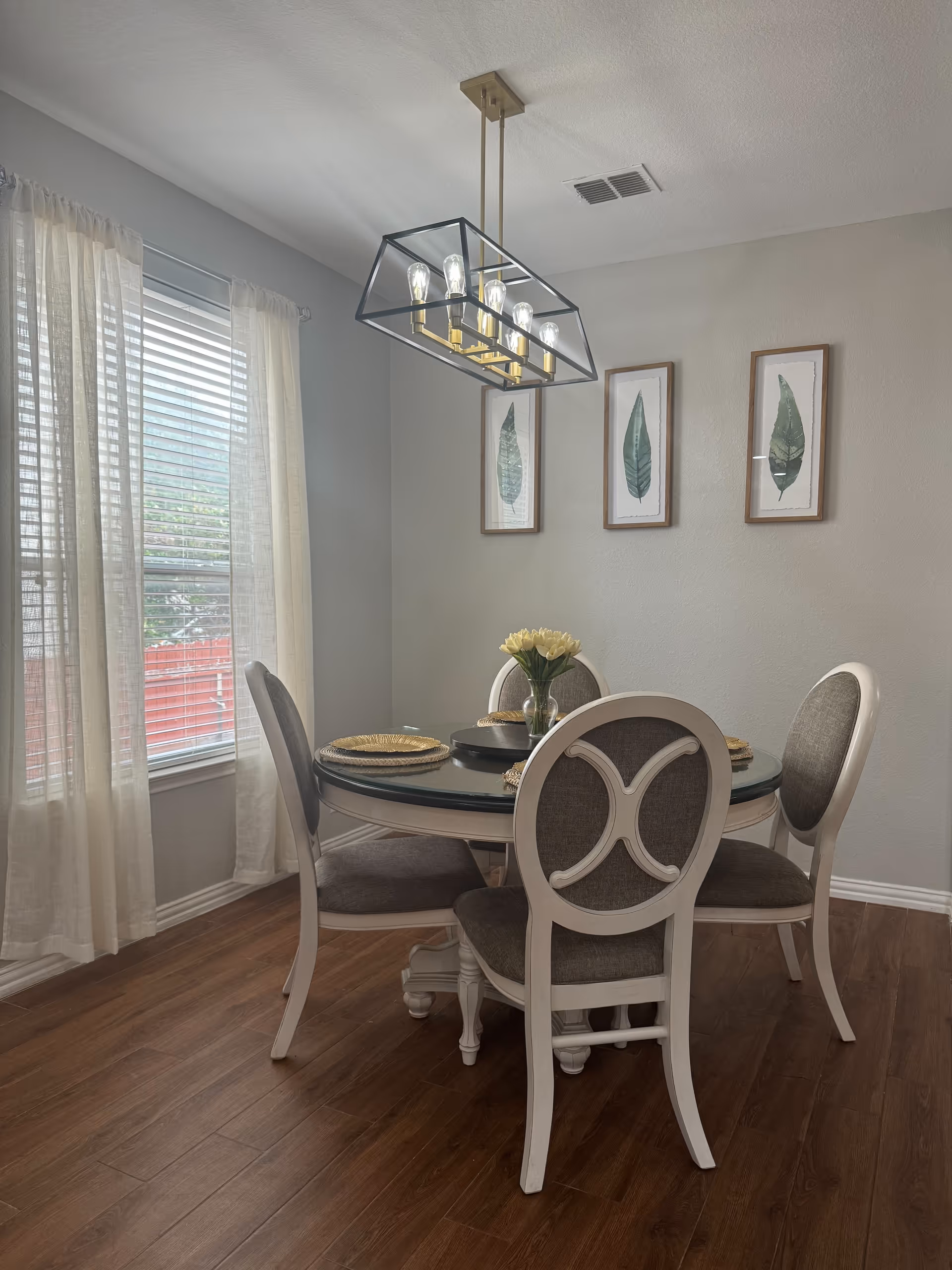 Light-filled dining room with a round table, chairs, chandelier, and wall art.