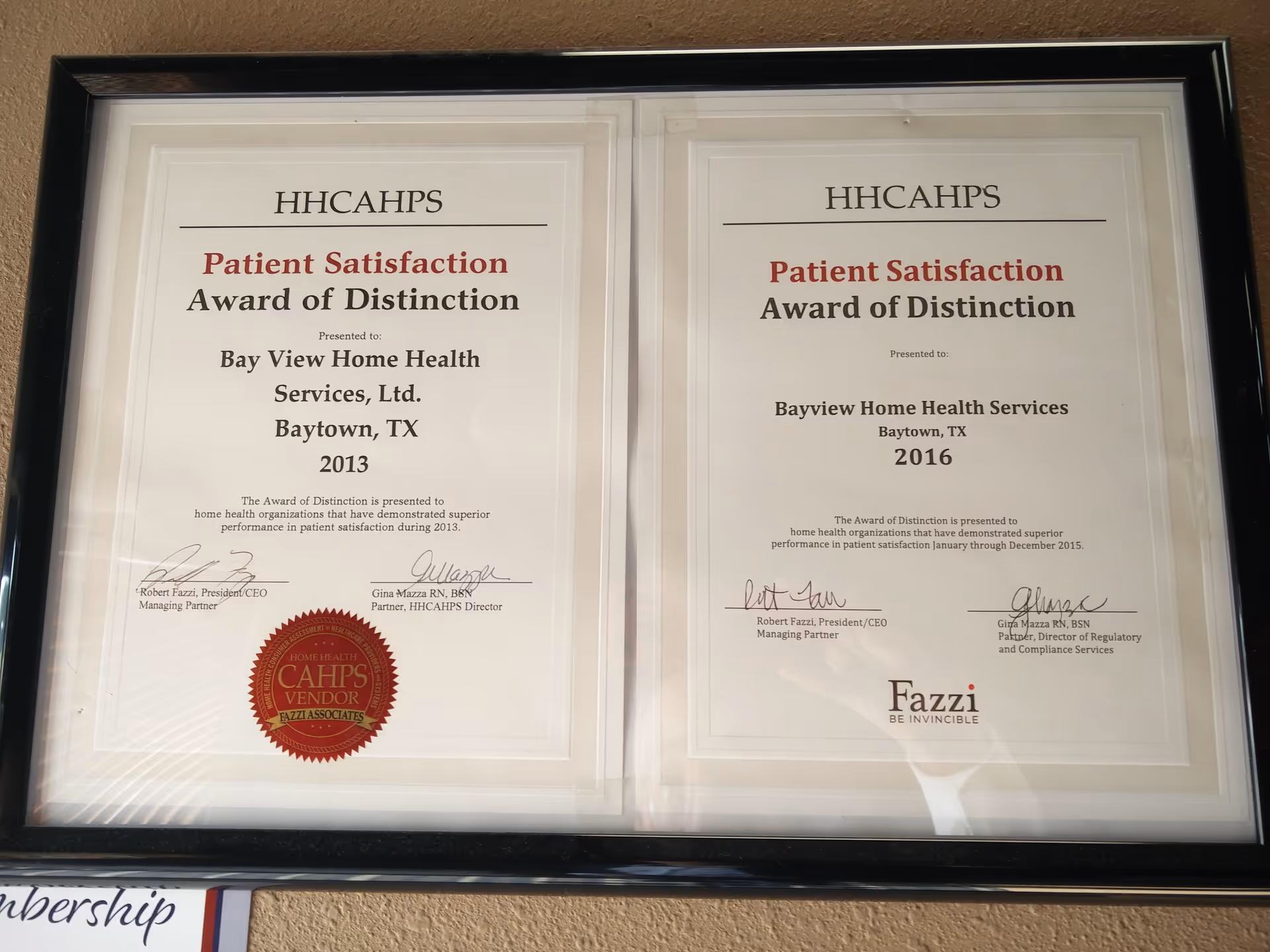Two framed certificates hanging side-by-side on a beige wall.