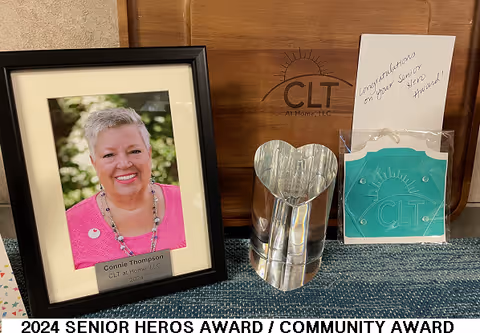 Framed portrait and award items on a table inside a facility, CLT at Home branding visible.