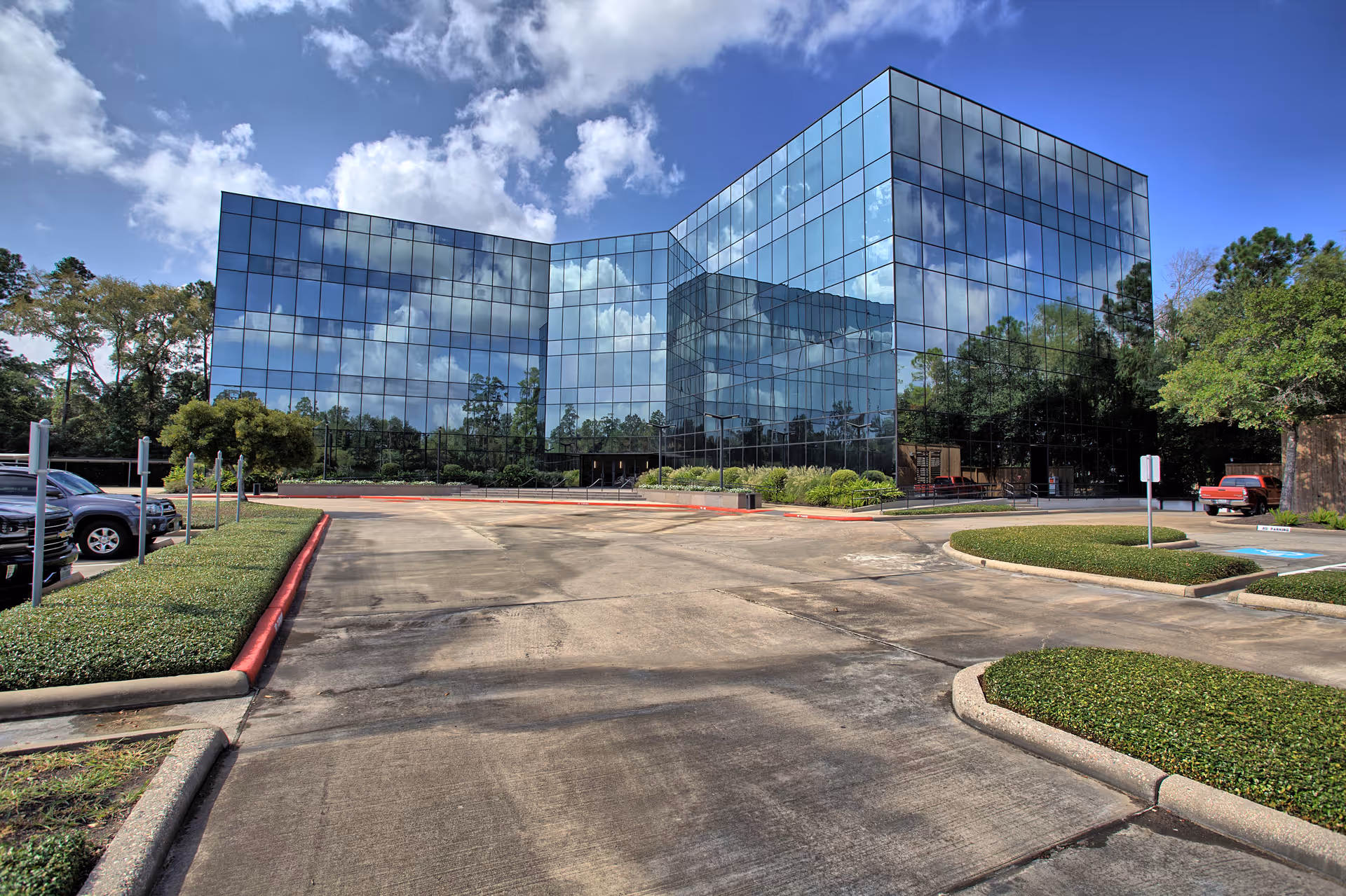 Modern glass-front building with reflective windows and a surrounding parking lot.