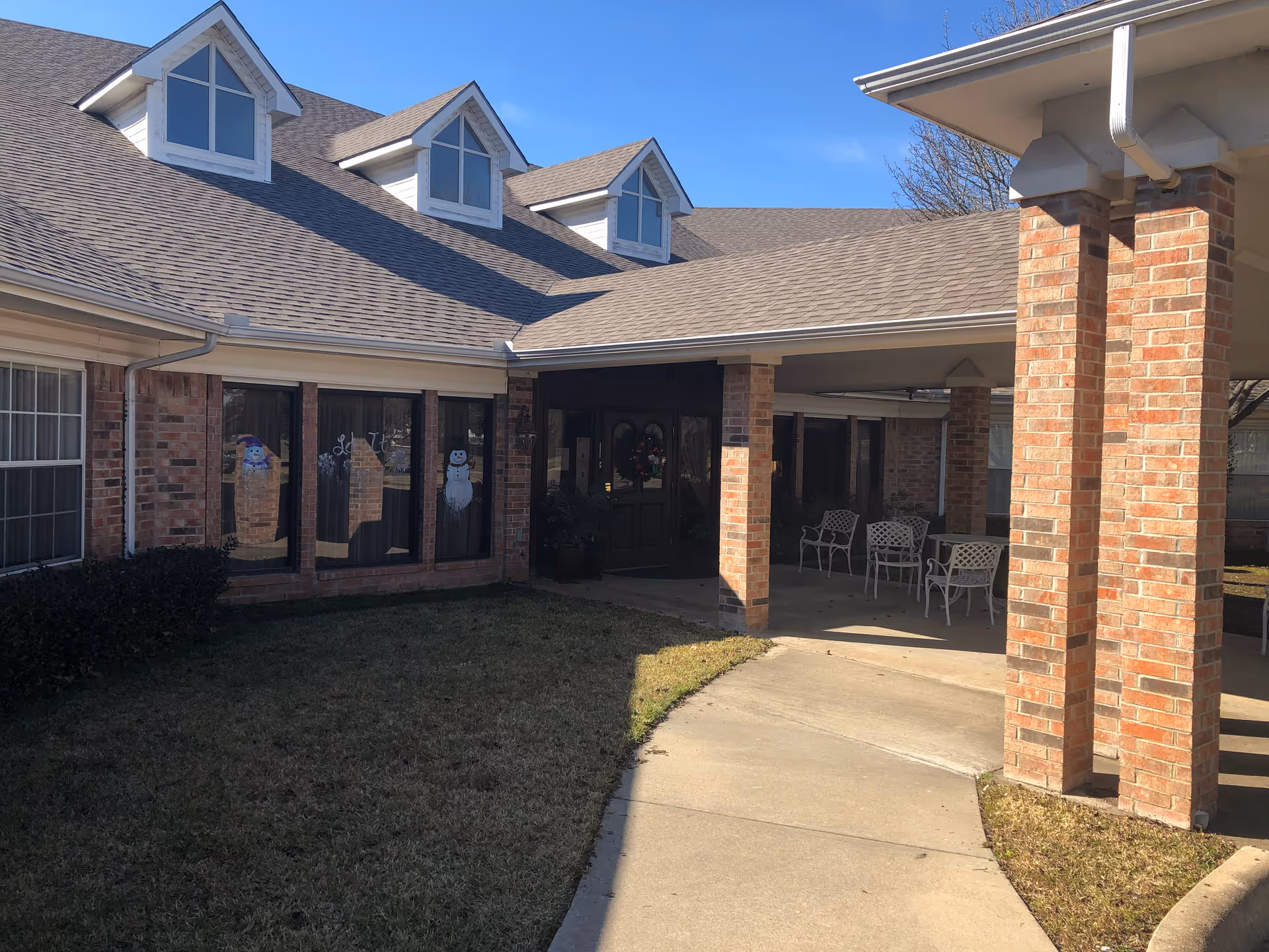 Crestwood Assisted Living exterior with brick columns, covered entrance, outdoor seating, and festive window decorations.