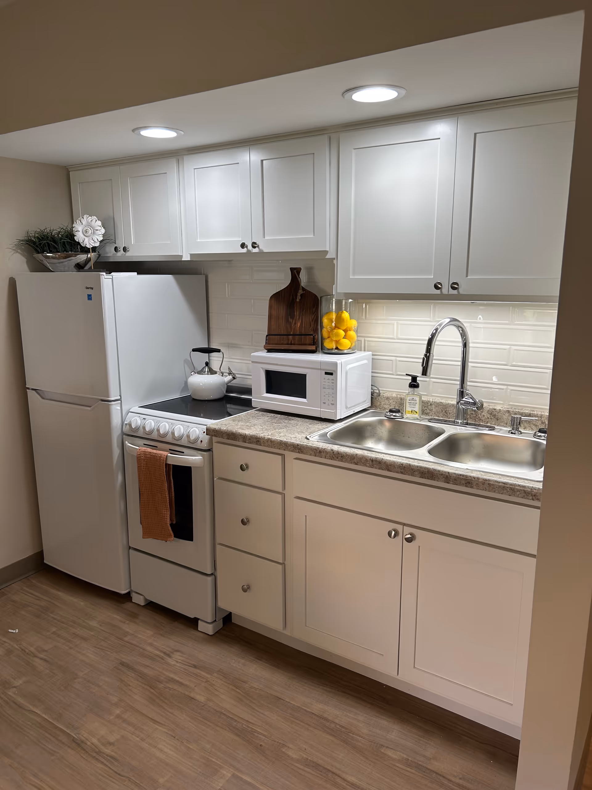 Compact white kitchen with refrigerator, stove, microwave, sink, and cabinets.