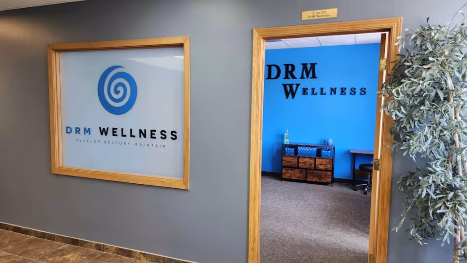 Interior hallway of DRM Wellness with framed logo on gray wall and blue doorway.
