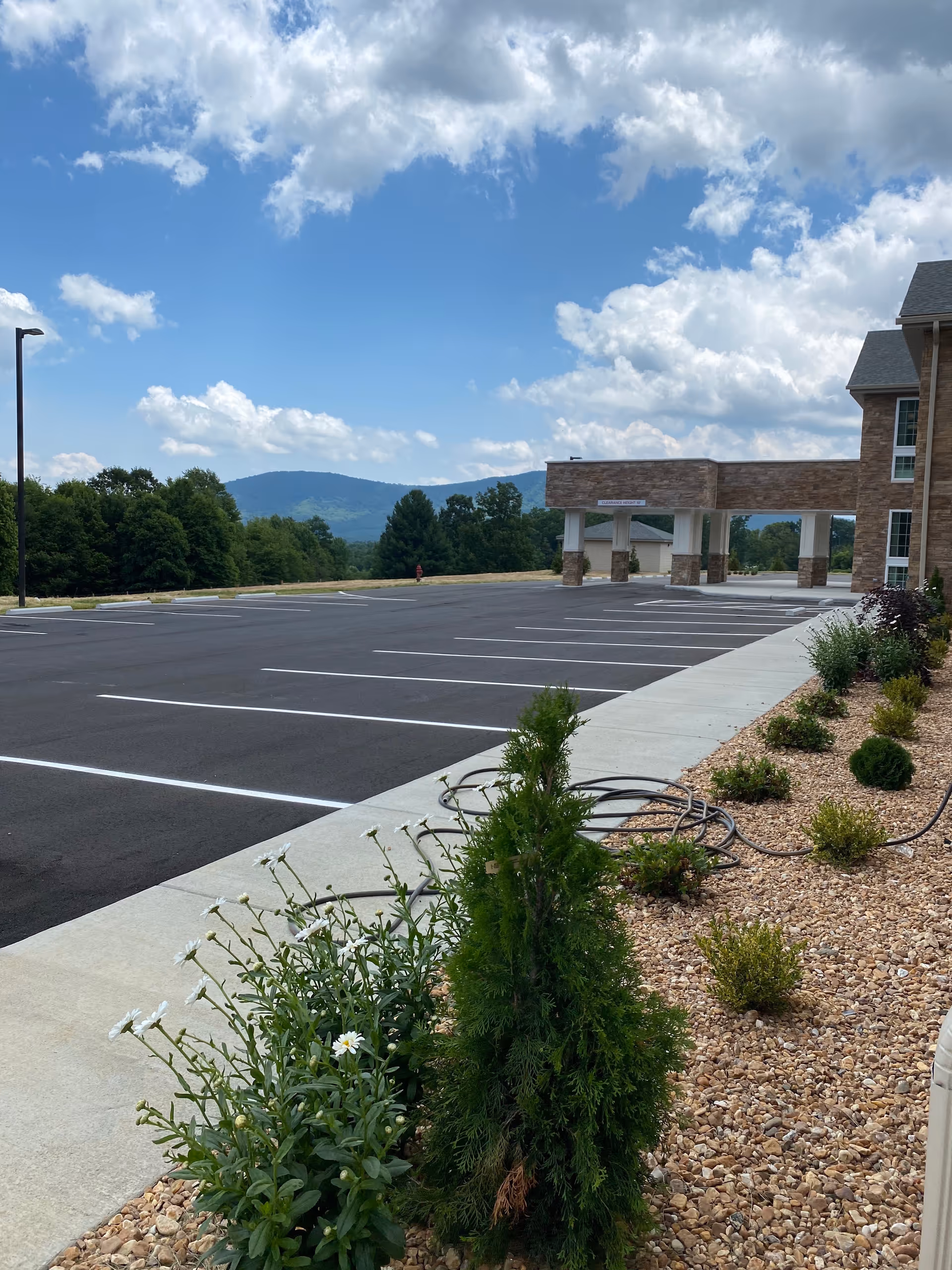Sunny exterior view of The Landings of Chestnut Grove with parking and landscaped shrubs.