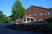 Brick senior living facility with covered entrance, trees, and landscaped driveway.