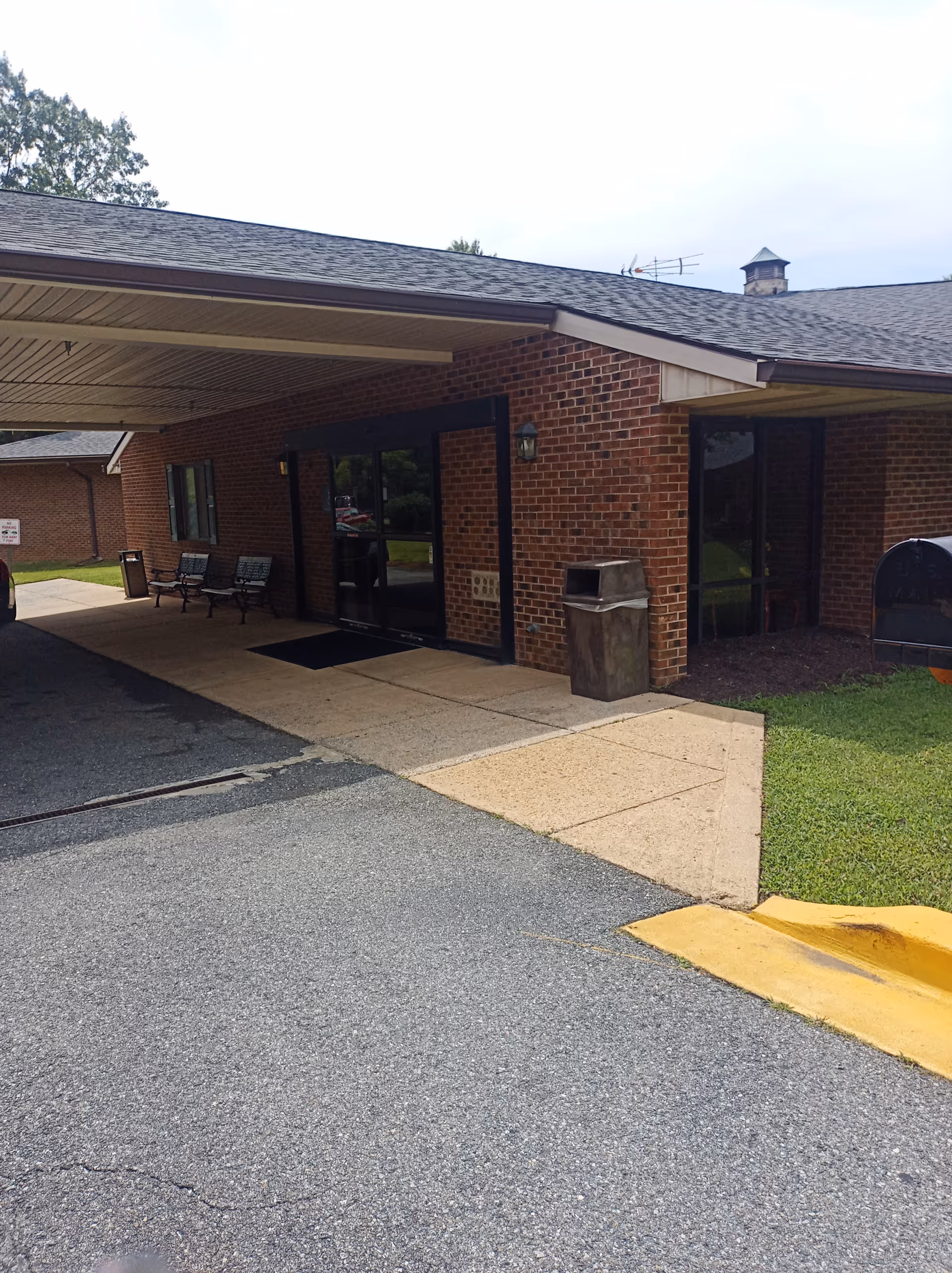 Brick senior living facility entrance with glass doors, covered front, and benches outside.