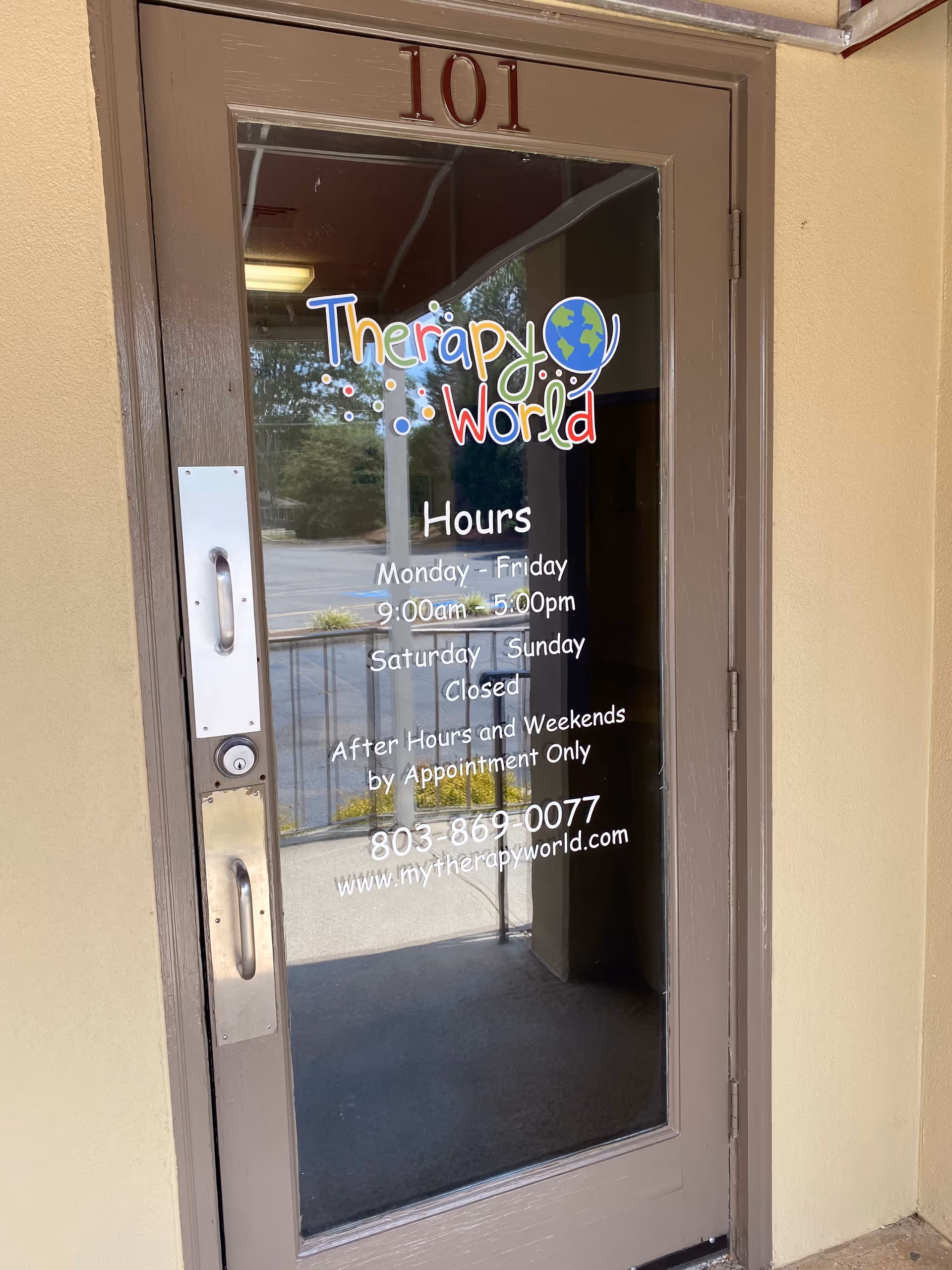 Glass door with Therapy World logo and hours, part of a building entrance.