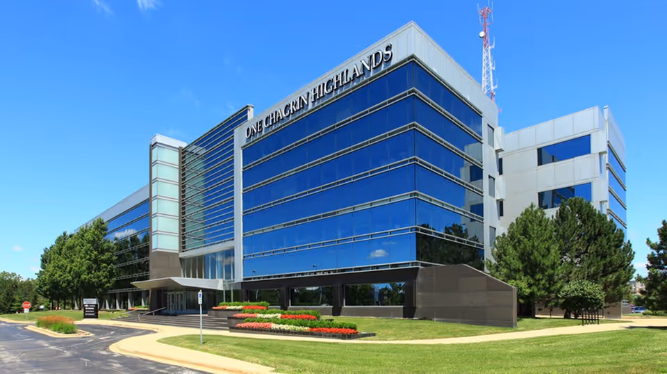 Modern glass-front office building with manicured lawn under a clear blue sky.