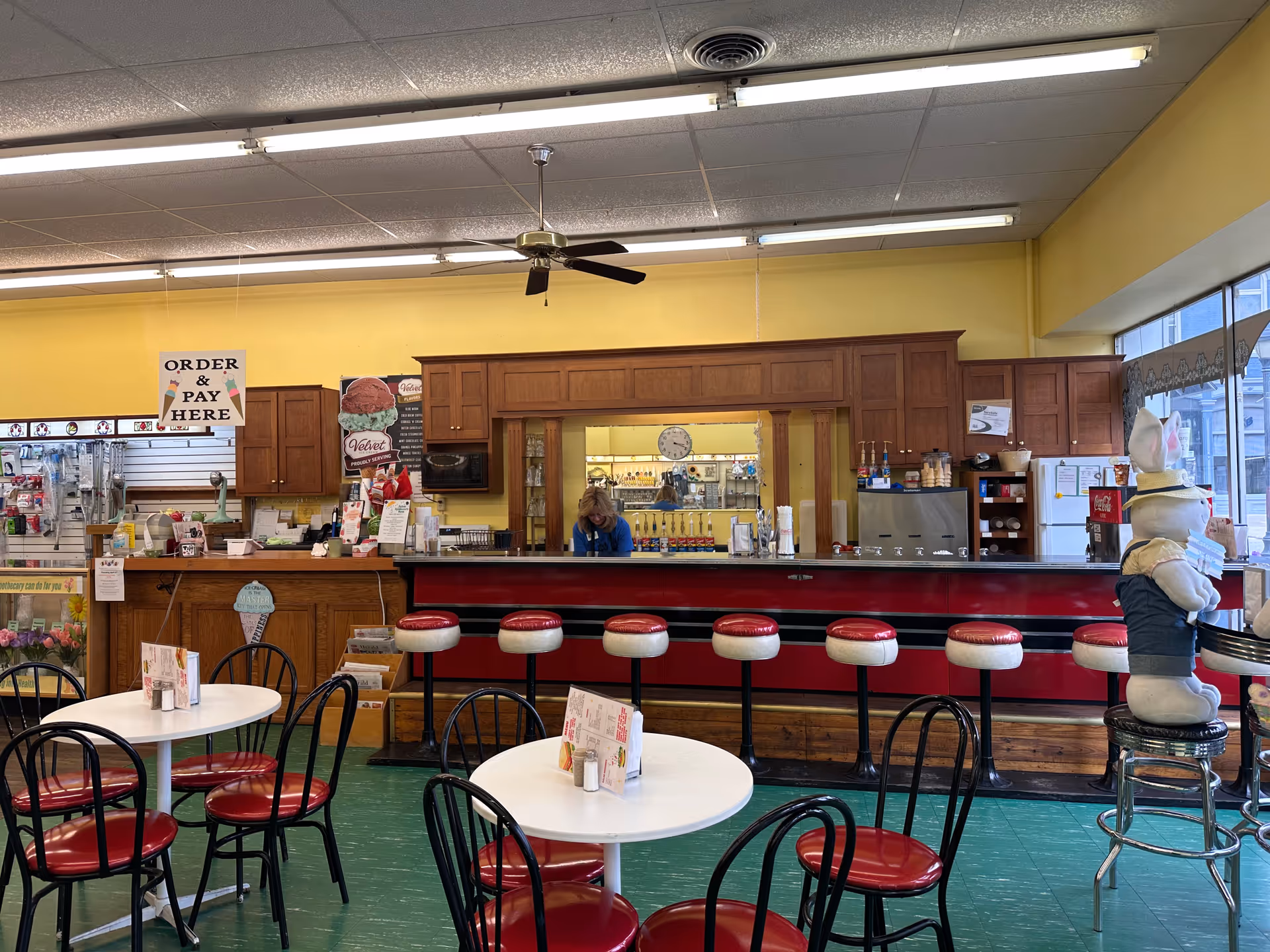 A retro café-style dining area with red stools, round white tables, and a service counter.