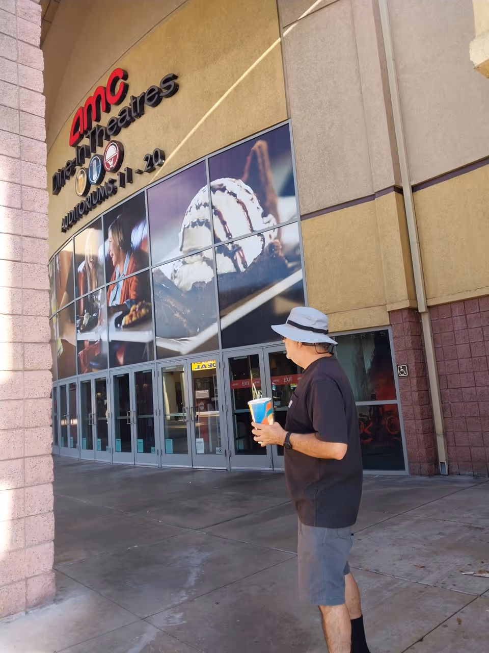 Man wearing a hat holds a beverage outside AMC Theatres entrance.