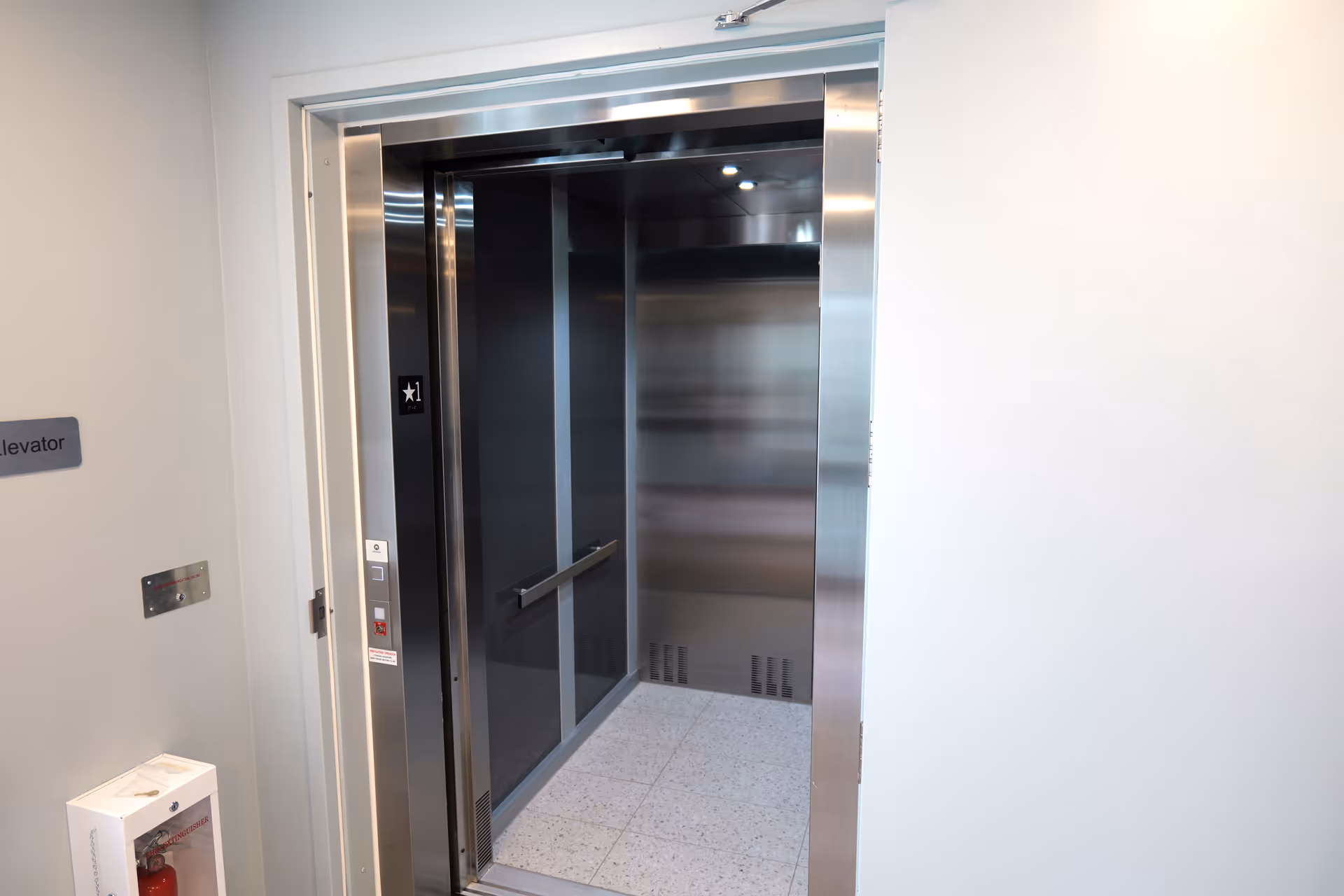 Stainless elevator doors open in a clean hallway with a tiled floor.