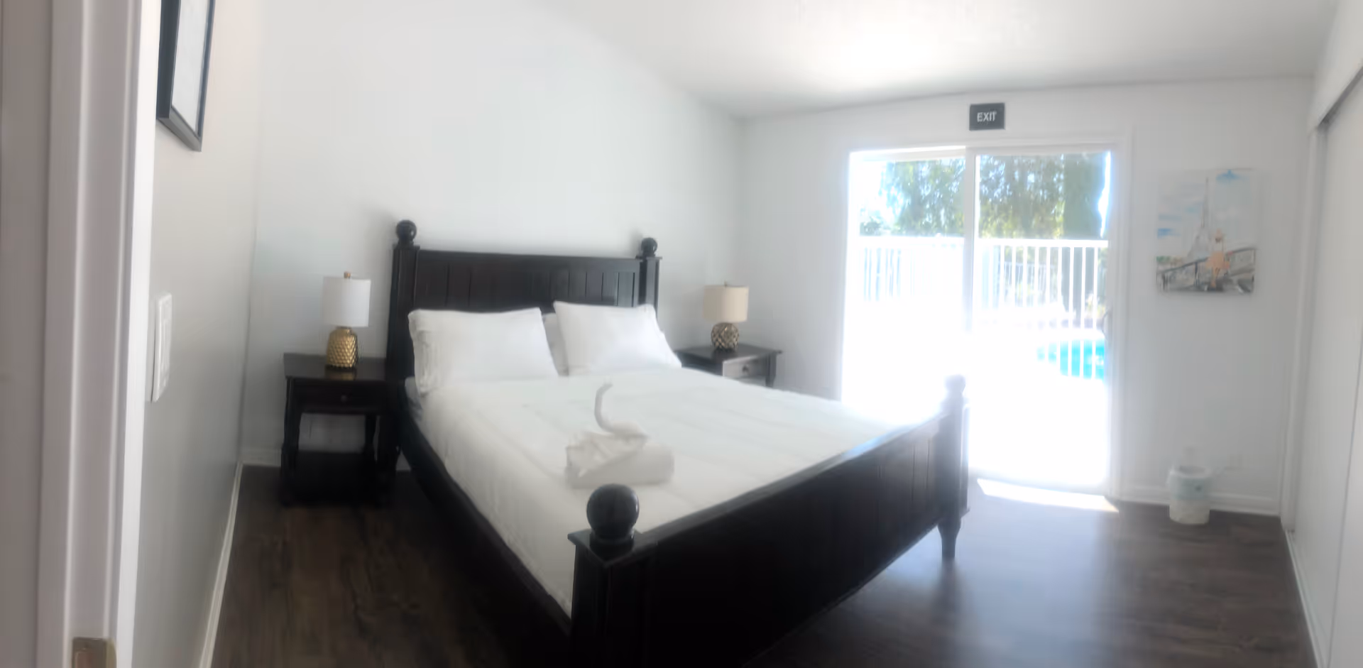 Dark wooden bed with white linens sits in a bright bedroom with two nightstands.