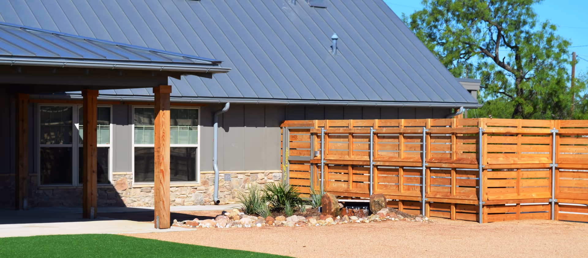 Exterior view of a modern facility with a wooden fence, stone accents, and garden rocks.