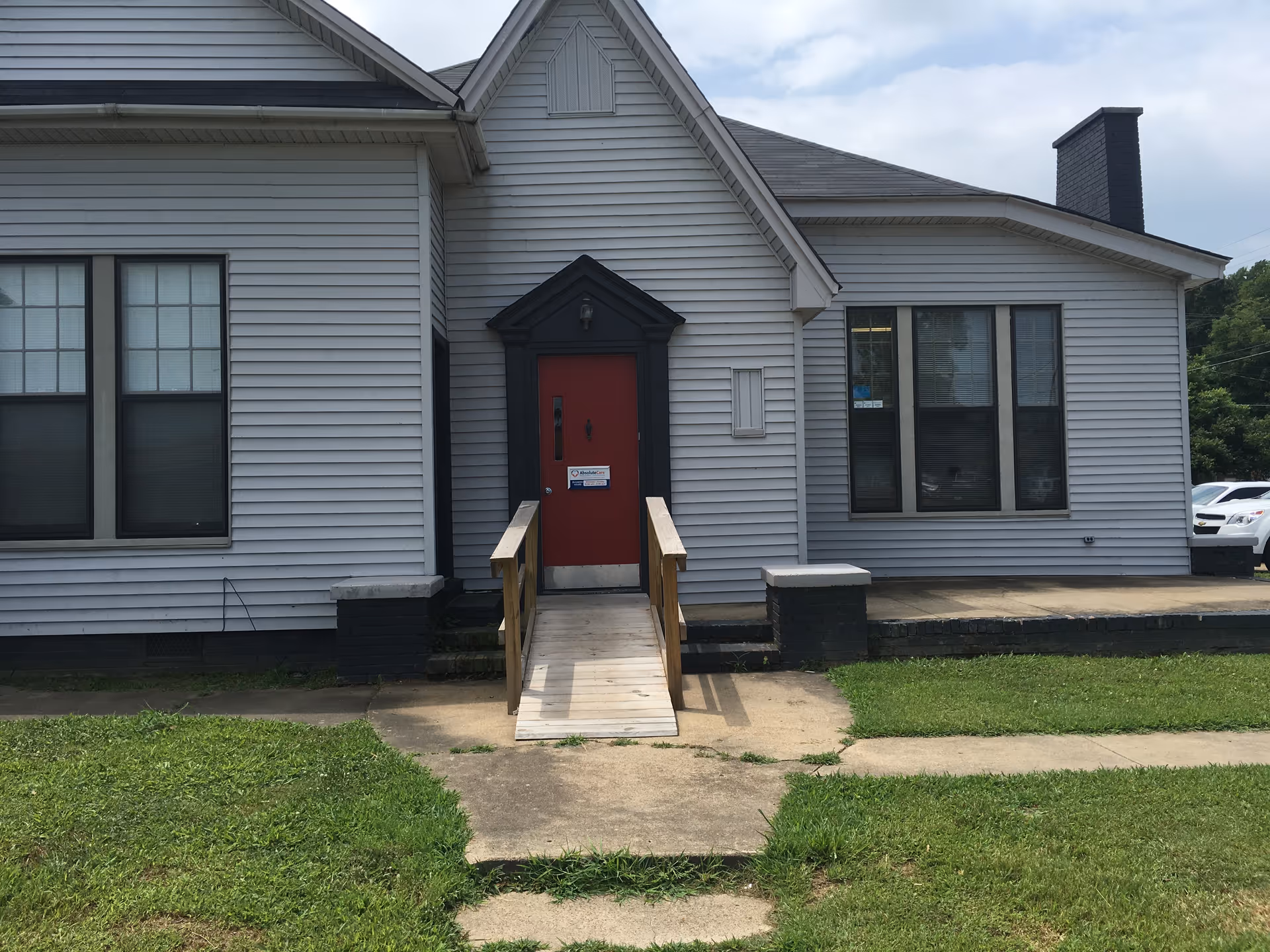 Exterior view of a gray single-story building with a red front door and ramp.