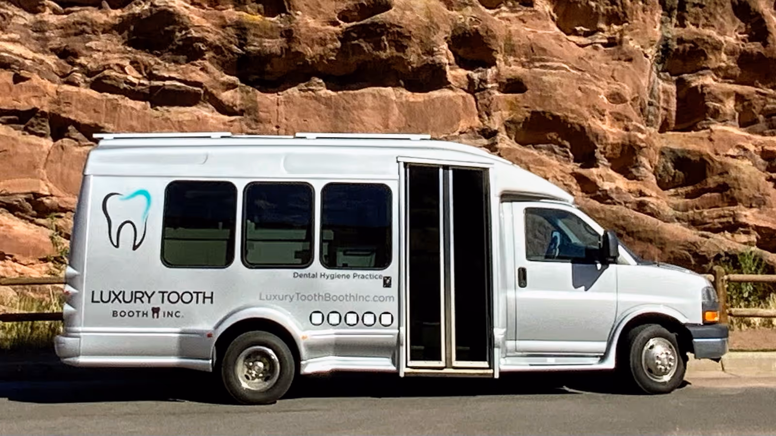 White dental van branded Luxury Tooth Booth Inc. parked beside a rocky hillside.