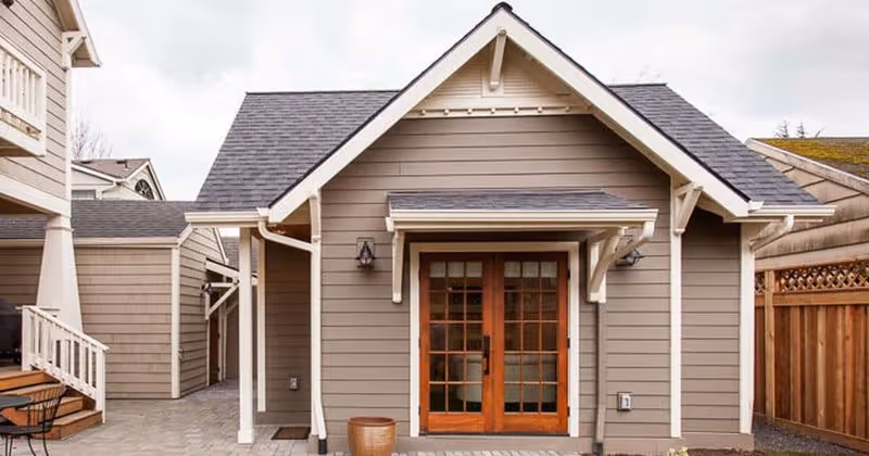 Gray-siding senior living facility exterior with white trim and wooden double doors at the entrance.