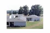Aerial view of gray-roofed senior living buildings on a green lawn with trees.