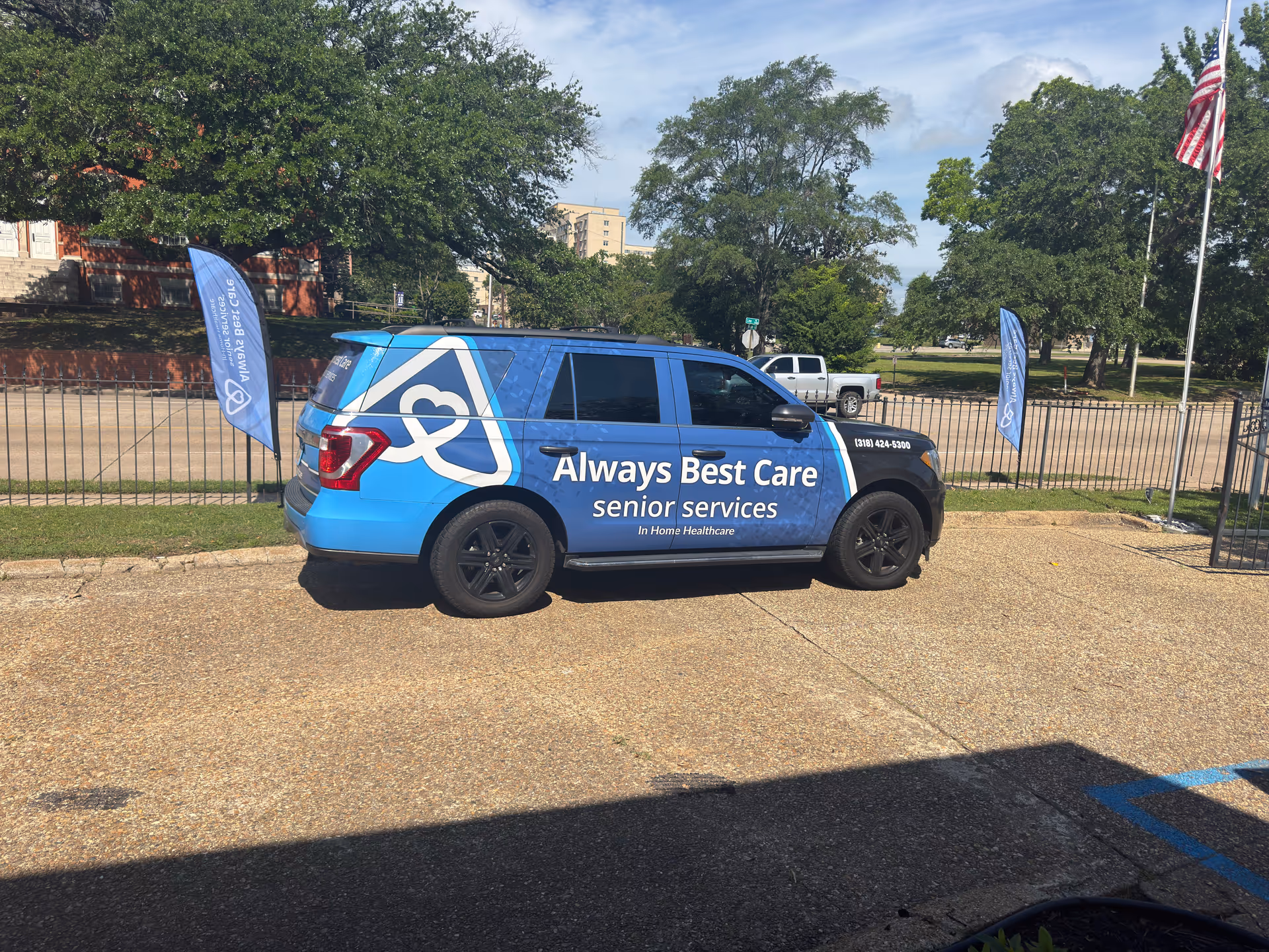 Blue van labeled Always Best Care parked outside with flags and trees