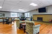 A spacious senior living common area with chairs, tables, and a fireplace.
