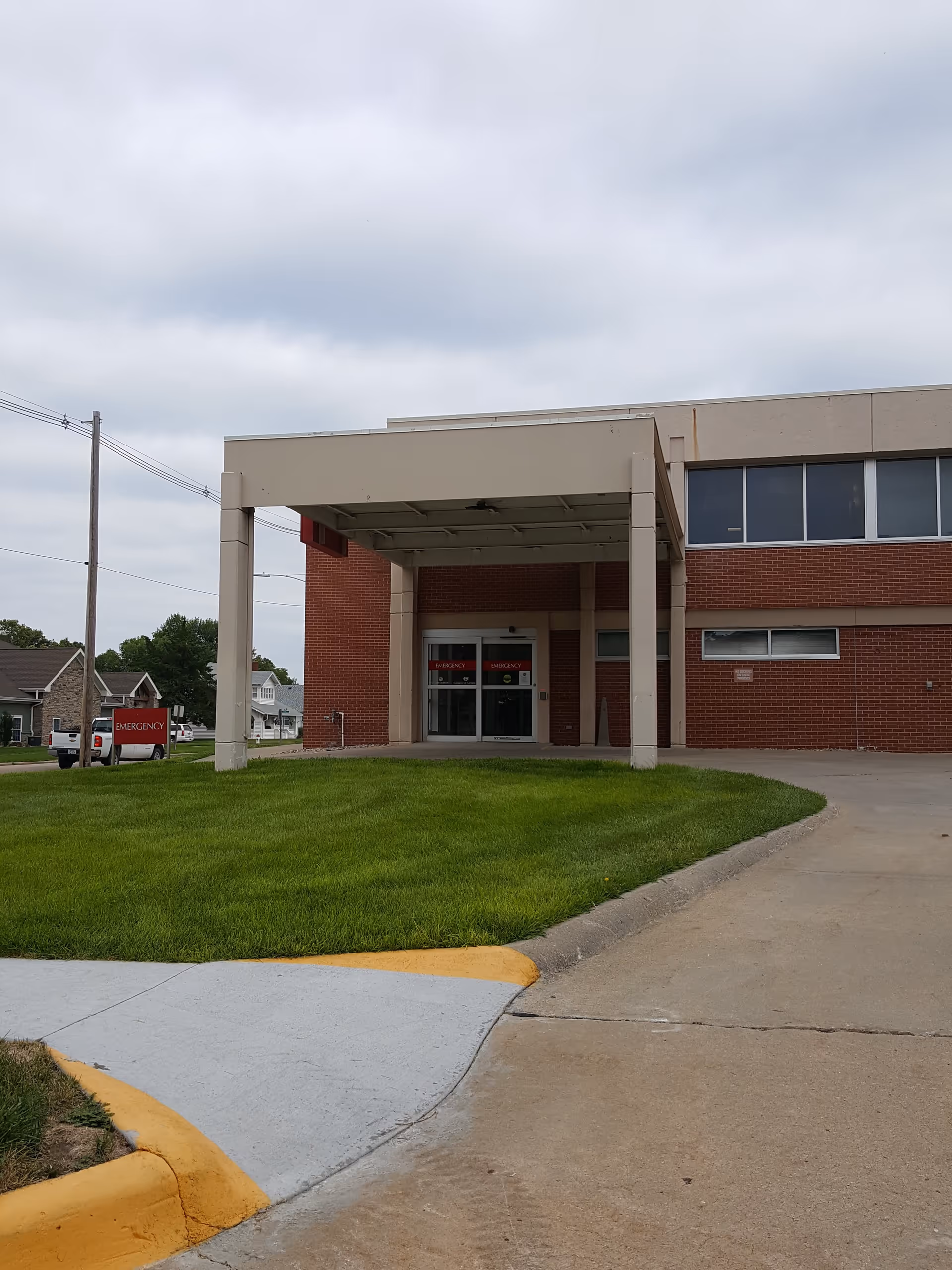 Glass doors under a pale canopy at a brick hospital entrance with a green lawn.