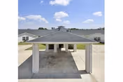 A covered carport with brick pillars stands before a low, light-gray senior facility building.
