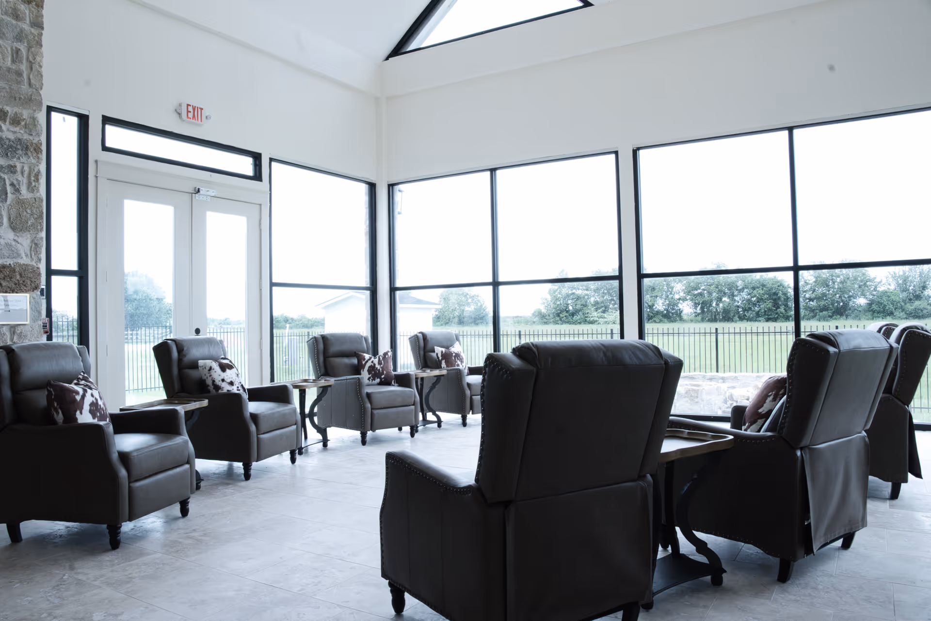Bright interior lounge with several dark leather recliners, small tables, and large windows.