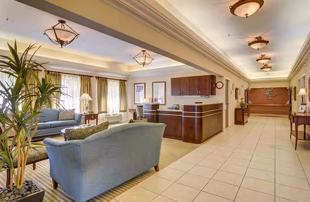 Spacious interior lobby featuring a curved dark wood reception desk, seating, and plants.